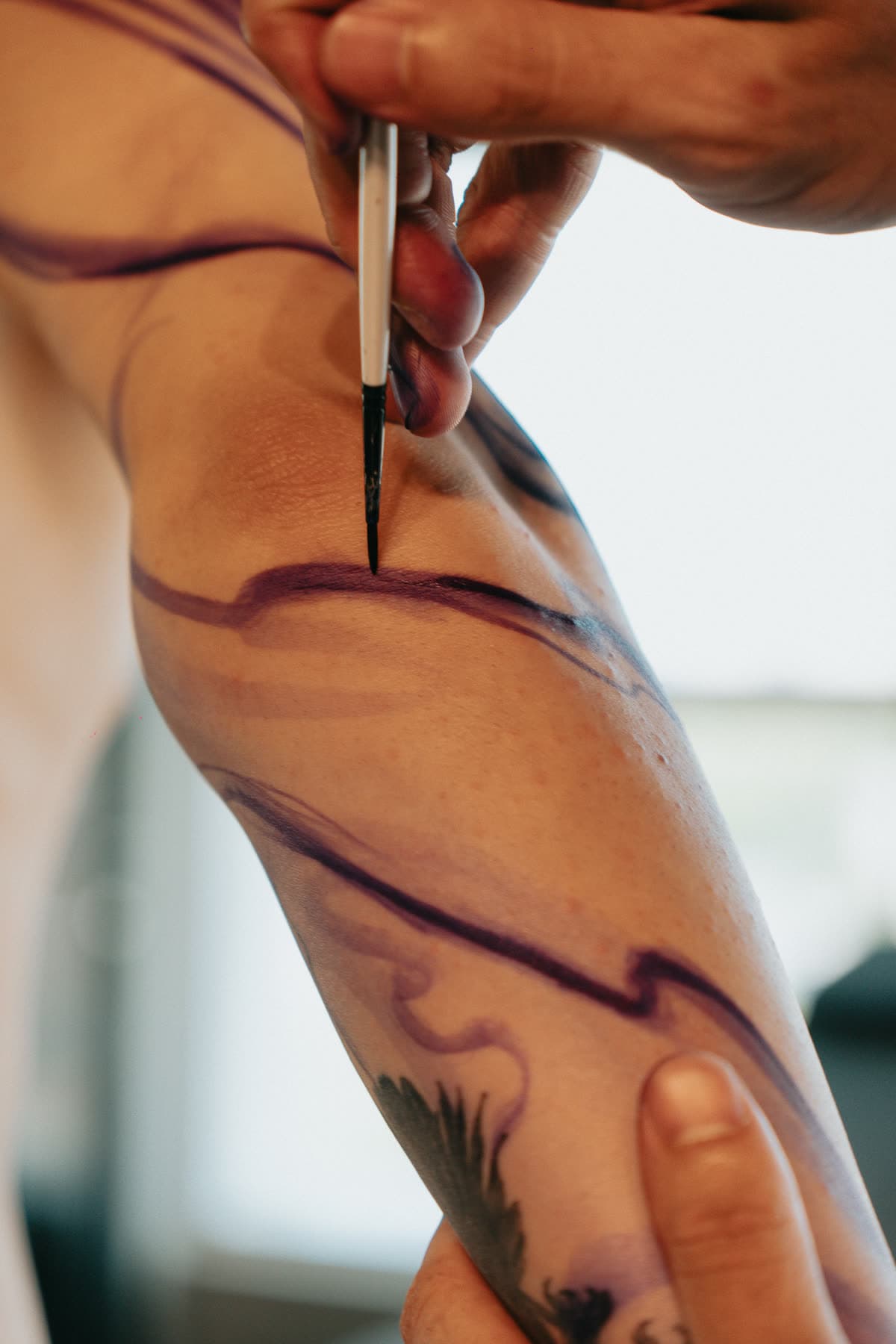 Close: a caneta correndo pelo antebraço, traço roxo sobre a pele