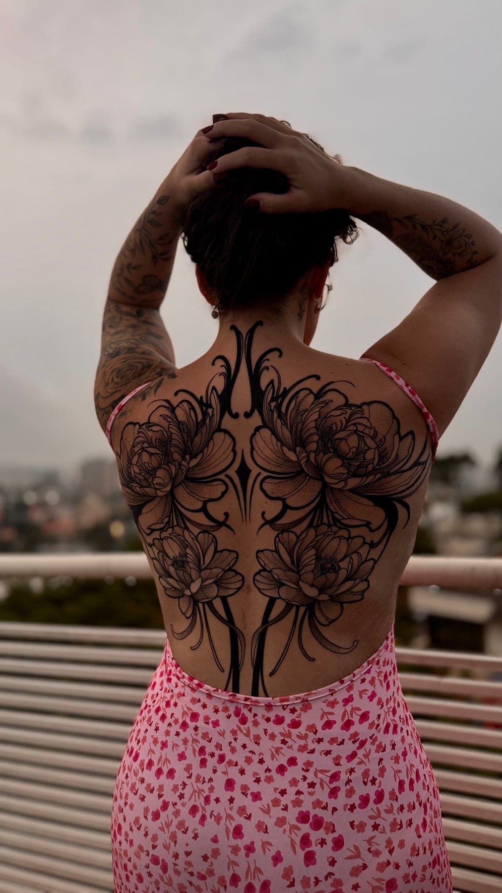 Costas femininas em blackwork: dois florais grandes abertos sobre as escápulas, a cidade ao fundo