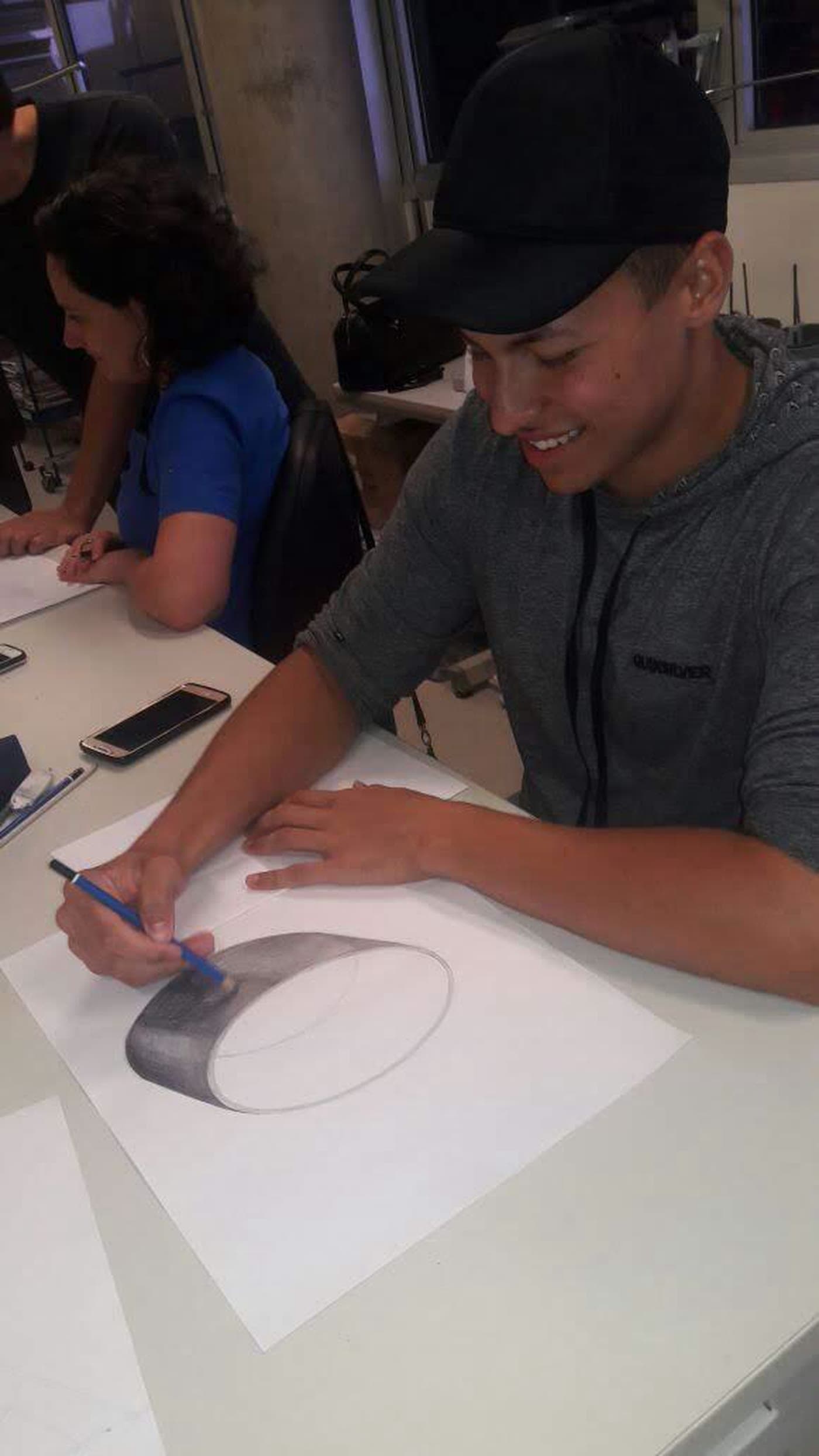 Cláudio no curso de tatuagem, desenhando numa folha sobre a mesa